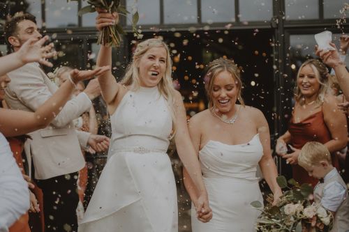 Two women celebrating at their LGBTQI+ wedding in the North East of England. They are both holding flowers and hands, walking through their guests laughing while everybody throws confetti. Concept for Surviving a Second Marriage (or Why Second and Third Marriages Often End in Divorce).