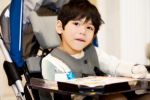 Disabled four year old boy studying or reading in wheelchair