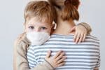 Little boy in a medical mask hugging his mother